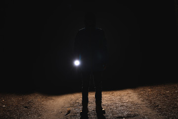 silhouette of man with bright flashlight in forest at night