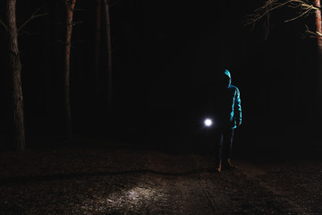 Man with bright flashlight in forest at night