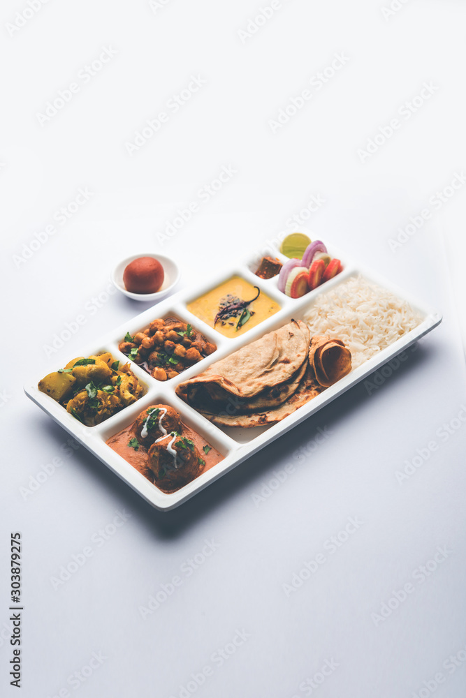 Indian vegetarian Food Thali or Parcel food-tray with compartments in which Malai Kofta, chole, Dal tarka, dry aloo sabji, chapati and rice with sweet gulab jamun served