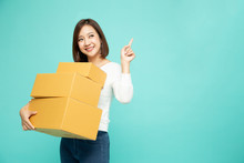 Happy Asian Woman Holding Package Parcel Box And Pointing Finger To Empty Copy Space Isolated On Light Green Background, Delivery Courier And Shipping Service Concept