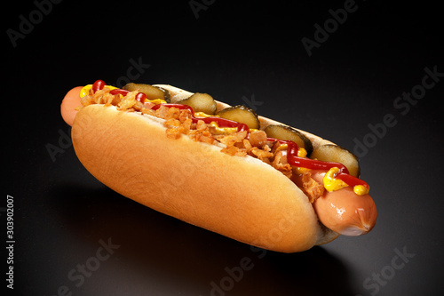 Cuadros en Lienzo Danish hot dog with pickled cucumbers, fried onions, ketchup and mustard on a black background