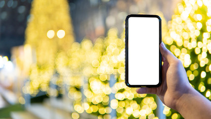 Male hand taking photo of illuminated Christmas tree and reindeer in Xmas holiday and New Year celebration event from smartphone. Mobile camera app for festive season. White blank device screen