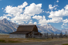 Deserted Wooden Barn On The Prairy With Mountains And A Cloudy Sky In The Background