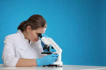 Poster - Scientist using modern microscope at table against blue background, space for text. Medical research