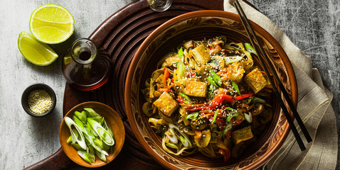 Wall Mural - banner of Asian vegan stir fry with tofu, rice noodles and vegetables, top view.