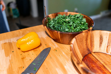 Cutting board table preperation with two large bowls of vegan salad with whole yellow orange bell pepper in kitchen and chopped green kale