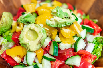 Chopped colorful vegetables in bowl macro closeup with fresh vegan salad with romaine lettuce and avocado half with bell peppers