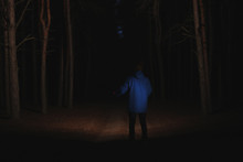 Man With Bright Flashlight In Forest At Night