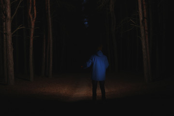 man with bright flashlight in forest at night