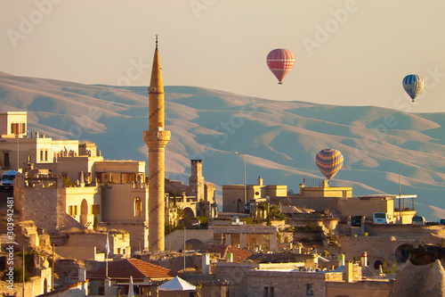 Fotografía Baloons ascending at sunrise over minaret and buildings of Cappadocia, Turkey,