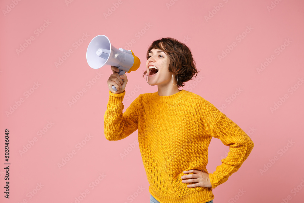 Funny young brunette woman girl in yellow sweater posing isolated on pastel pink wall background studio portrait. People sincere emotions lifestyle concept. Mock up copy space. Screaming in megaphone. - obrazy, fototapety, plakaty 