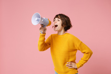 Funny young brunette woman girl in yellow sweater posing isolated on pastel pink wall background studio portrait. People sincere emotions lifestyle concept. Mock up copy space. Screaming in megaphone.