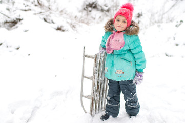 Wall Mural - Lovely smiling girl with frozen sled in her hand posing for camera in winter snowy day outdoor.