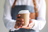 A waitress holding and serving a paper cup of hot coffee in cafe