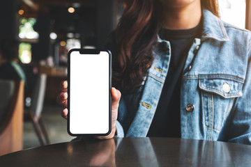 mockup image of a woman holding and showing black mobile phone with blank screen in cafe