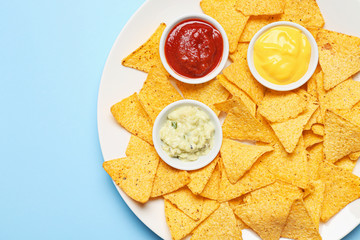 Plate with tasty nachos and sauces on color background