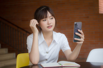 Wall Mural - Portrait of thai adult student university uniform beautiful girl using her smart phone Selfie