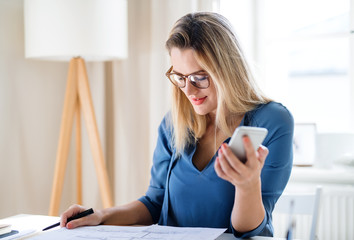 Young woman sitting at the desk indoors in home office, working.