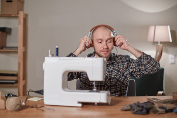 Happy man listen music and working with sewing machine in a textile studio. Tailor makes bow ties of woolen fabric.