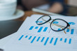 © semenenkostas - Workplace of the businessman. Vision glasses in focus and investment charts out of focus close up