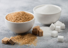 White Bowl Plates Of Natural Brown And White Refined Sugar And Cubes On Light Table Background.