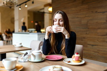 Young Woman Drinks Tea In A Cafe And Enjoys A Delicious Dessert