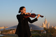 Beautiful female professional violinist playing outdoors on a violin in a black suit.