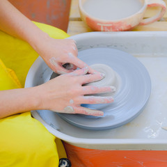 Female hands working with white clay on pottery wheel