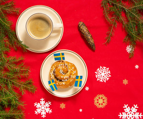 Wall Mural - Swedish cinnamon bun (kanelbull) and coffee cup. Swedish flags and red tablecloth. Coffee break (fika) concept. Christmas (Jul) concept. Top view.