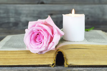 Burning White Candle And Pink Rose On Open Book