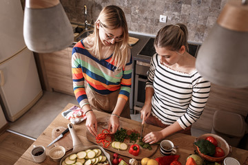 Two female friends  preparing vegetarian meal.They making fun a the kitchen and preparing vegetables.