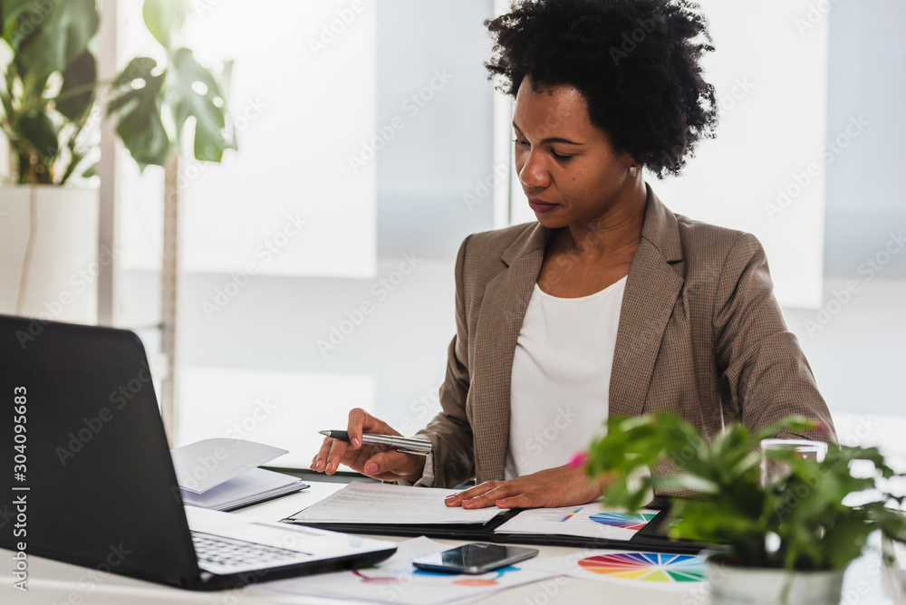 Serious african-american business woman working on laptop at office - obrazy, fototapety, plakaty 