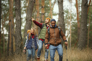 group of friends on a camping or hiking trip in autumn day. men and women with touristic backpacks g