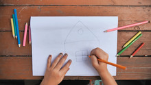 Child Draws A Pencil Drawing Of The House And His Family. New Home.