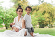 © ronnachaipark - Happy loving family. Asian young beautiful mother and her children, new born baby girl and a boy sitting on green grass to playing and hugging in the park