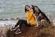 Young beautiful woman in yellow pullover sweater plays with a dog (grey and white husky) on the beach