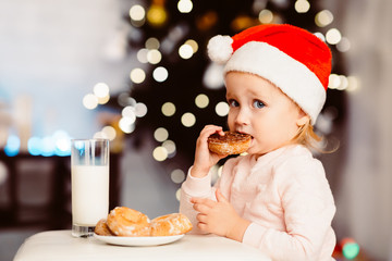 Baby girl eating cookie with milk near xmas tree