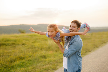 Wall Mural - Handsome young father in green sunny summer nature holding his cute small daughter in the arms.