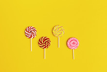 Sweet Round Candy Lollypops With Stripes On Stick On Yellow Paper Background. Creative Concept Still Life Sweets For Birthday, Party, Holidays. Top View And Flat Lay.