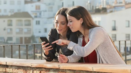 Wall Mural - Two friends talking checking mobile phone content in a balcony on holiday