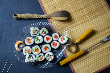 red fish sushi with rice filling, on a serving plate on a black background, top view