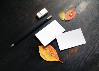 Photo of blank white business cards, pencil, eraser and autumn leaves on wood table background. Branding stationery set.