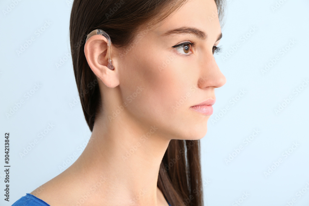 Young woman with hearing aid on color background
