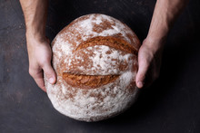 Man Baker Holds Bread In His Hands On Dark Background Top View
