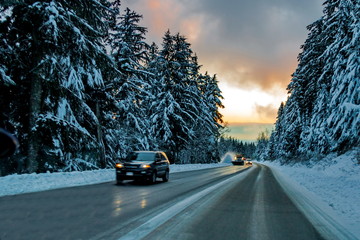 The icy Winter Road to the ski slopes of Seymour Mountains passes through a snowy forest, cars and a snow sweeper truck are moving up the road, Mountain Seymour Provincial Park