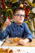 Uśmiechnięty chłopiec podczas Świąt Bożego Narodzenia siedzi przy stole i zjada świąteczne danie.