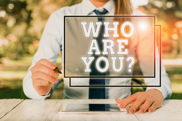 Text sign showing Who Are You Question. Business photo showcasing Identify yourself description demonstratingal characteristics Female business person sitting by table and holding mobile phone