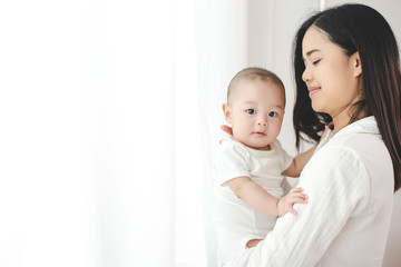 the mother hugged the child by the window and the curtain shone brightly. her child looked at the ca