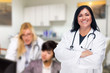 © Andy Dean - Handsome Hispanic Doctor or Nurse Standing in Her Office with Staff Working Behind
