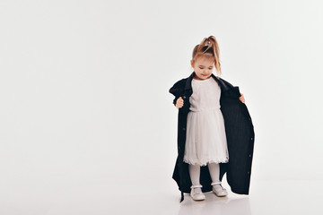 a little girl tries on dad's shirt. Child in big black clothes on white background. Concept of children's games, imitation of adult life, fashion